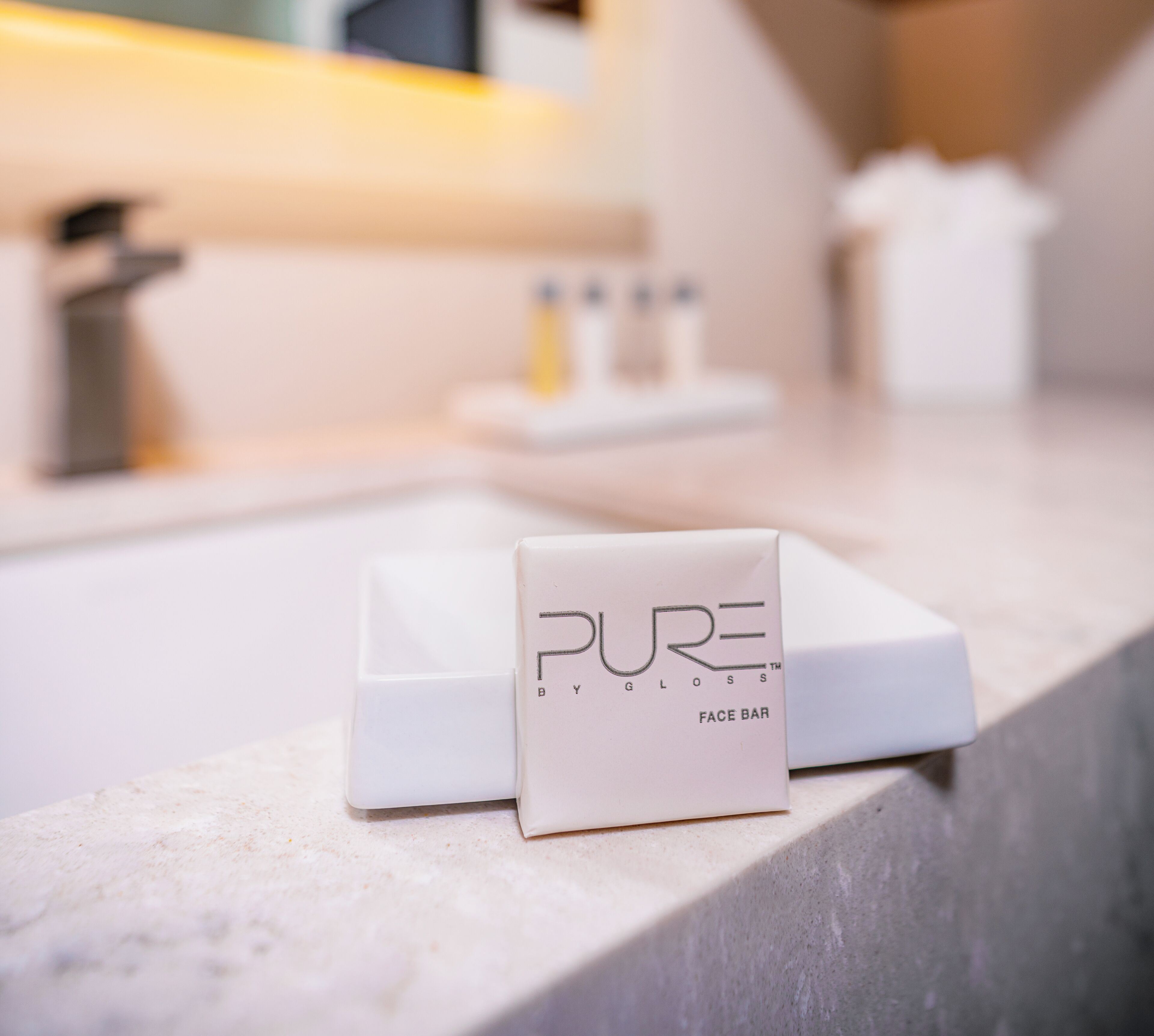 Een badkamer met een wit wastafelmeubel, een spiegel en een zeepdispenser met de tekst 'PURE GLOSS'.
