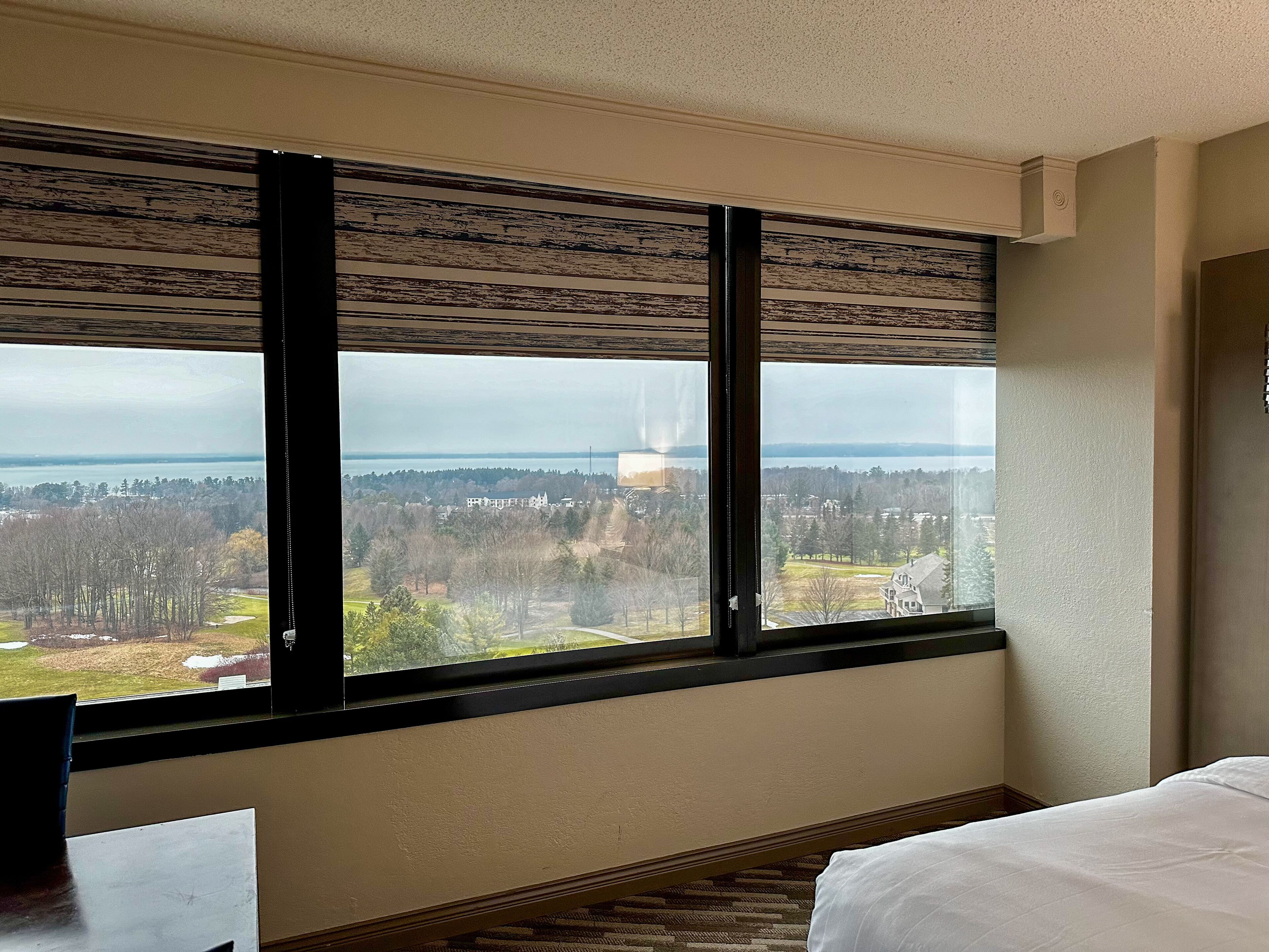 A hotel room with a large window offering a view of a residential area and a body of water.