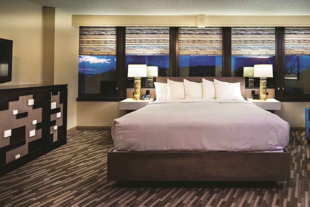 A hotel room with a large bed, two bedside lamps, a TV, a sofa, and a patterned rug.