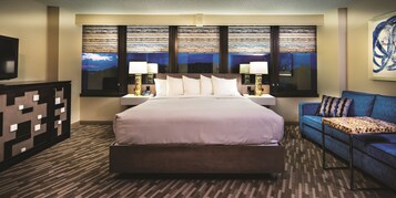 Una habitación de hotel con una cama grande, dos lámparas de noche, un televisor, un sofá y una alfombra estampada.