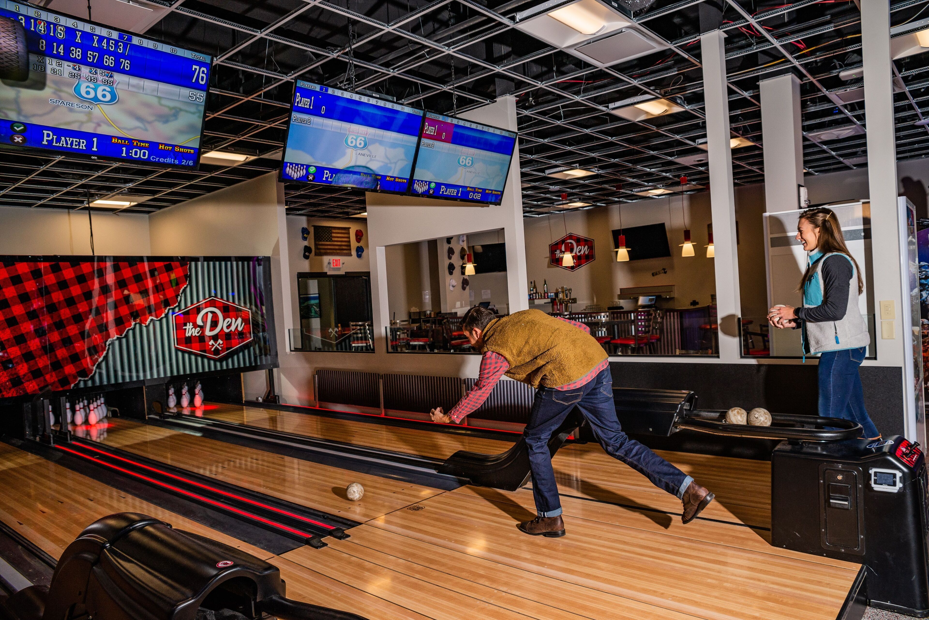 A bowling alley with multiple lanes, a bowling ball in motion, and overhead scoreboards.
