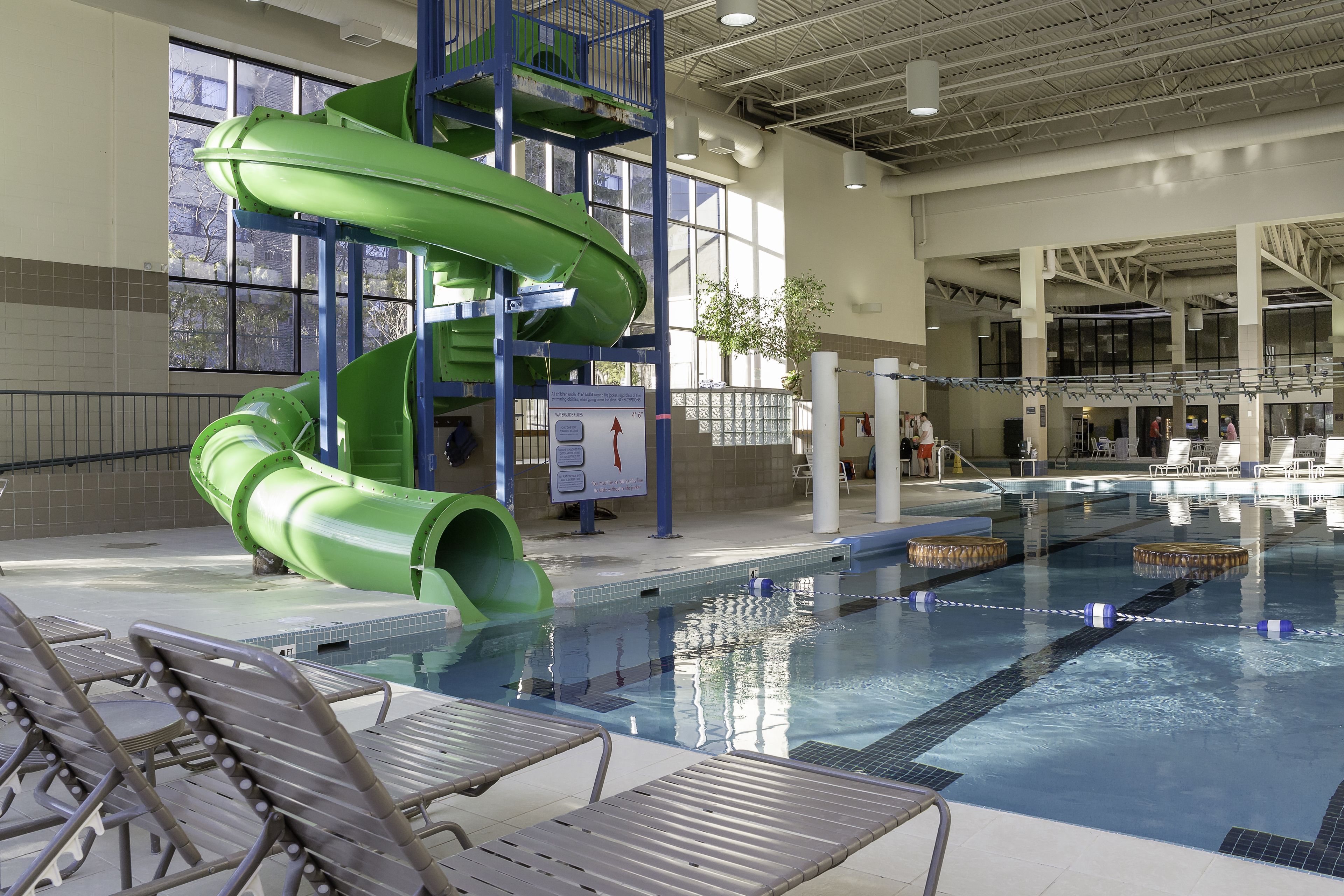 Une piscine avec un toboggan aquatique vert, des chaises longues et une vue dégagée sur l’ensemble de la piscine.