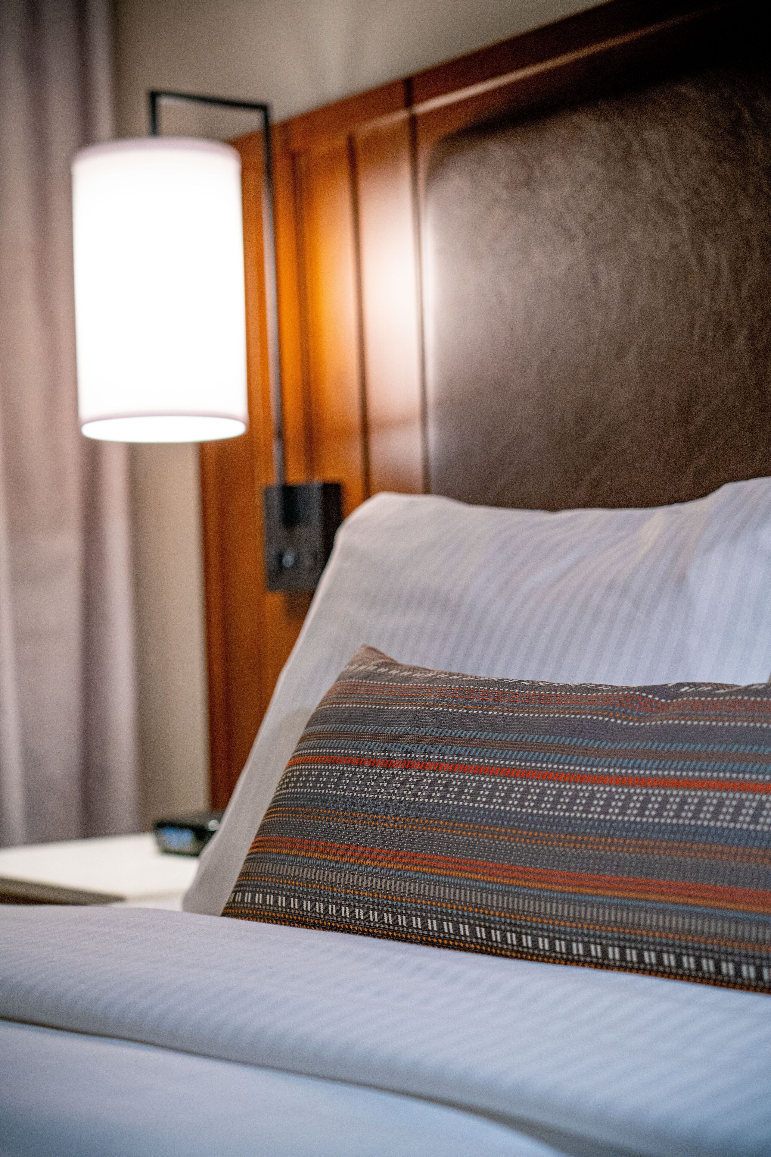 Un lit bien fait, avec un oreiller à motifs, une lampe de chevet et une tête de lit en bois.