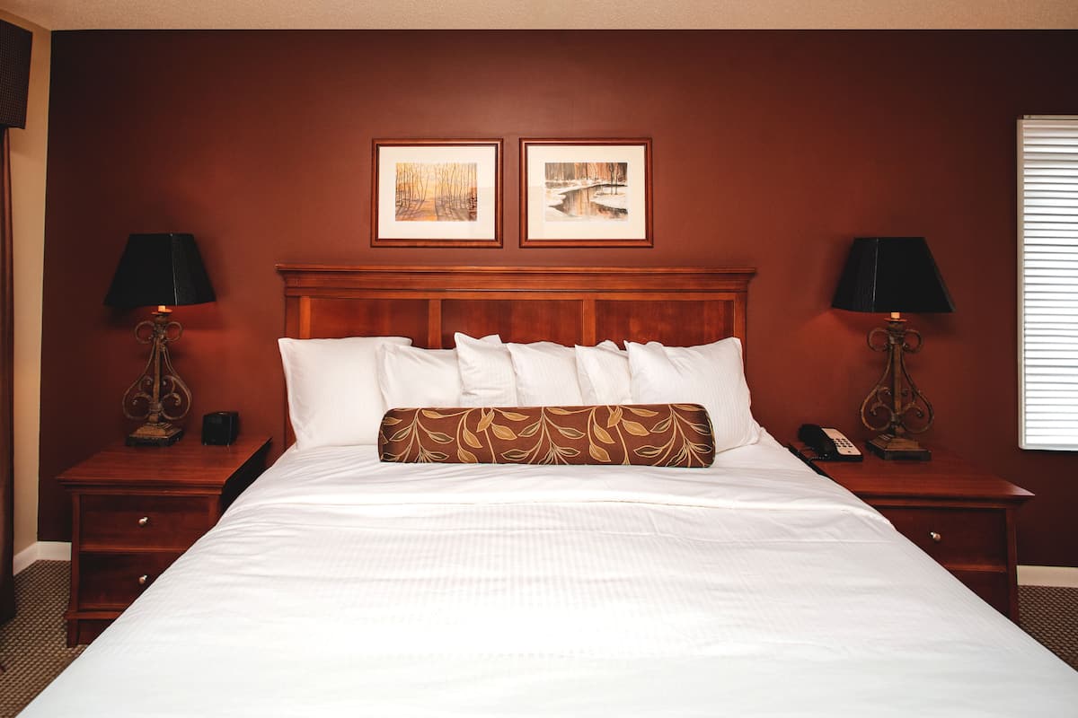 A hotel room with a large bed, two bedside tables, a wooden headboard, and two framed pictures on the wall.