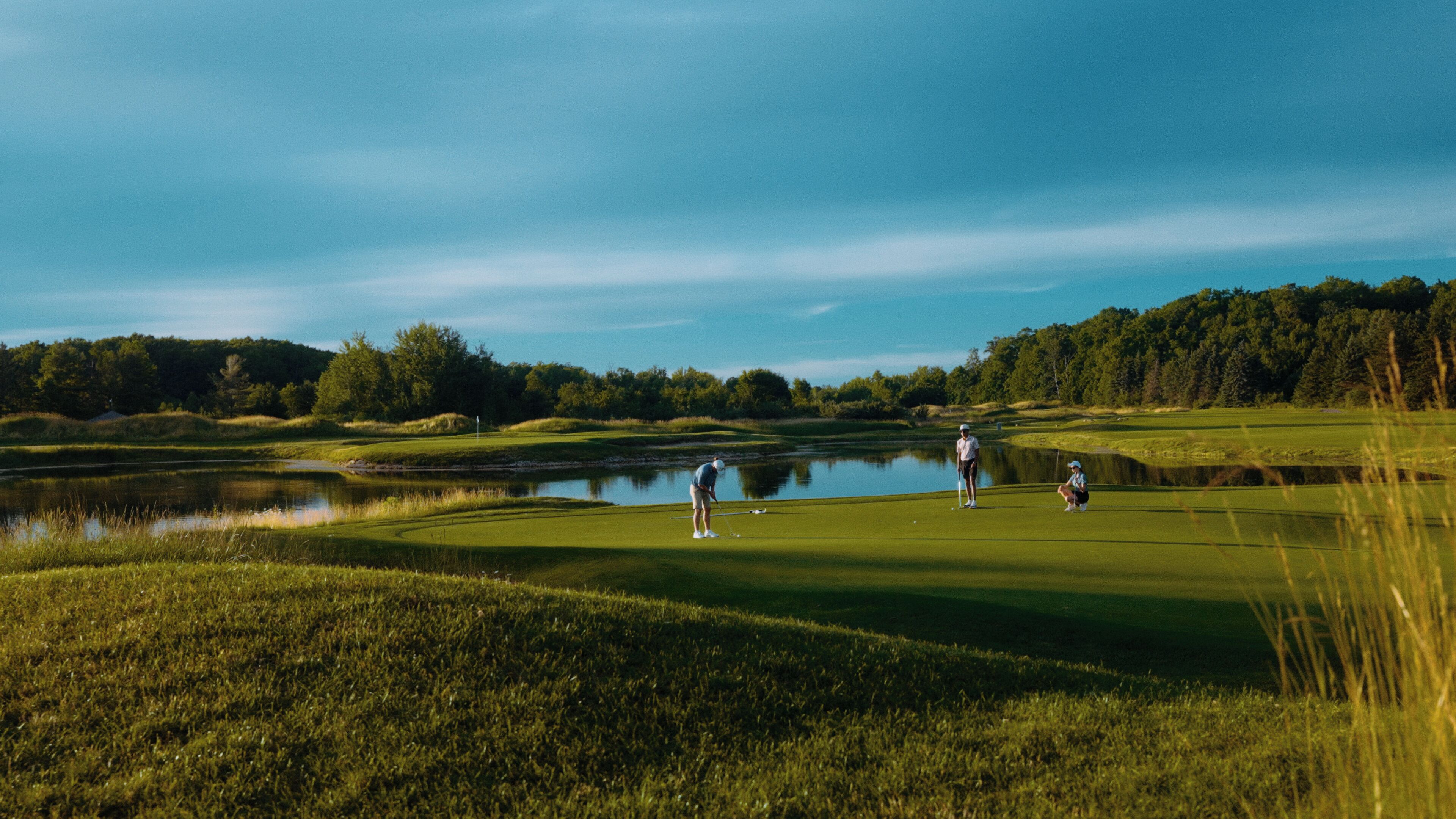 A golf course with a pond, trees, and a clear sky.