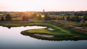 A golf course with a pond, sand bunkers, and a water tower in the background. - Grand Traverse Resort And Spa (Williamsburg)