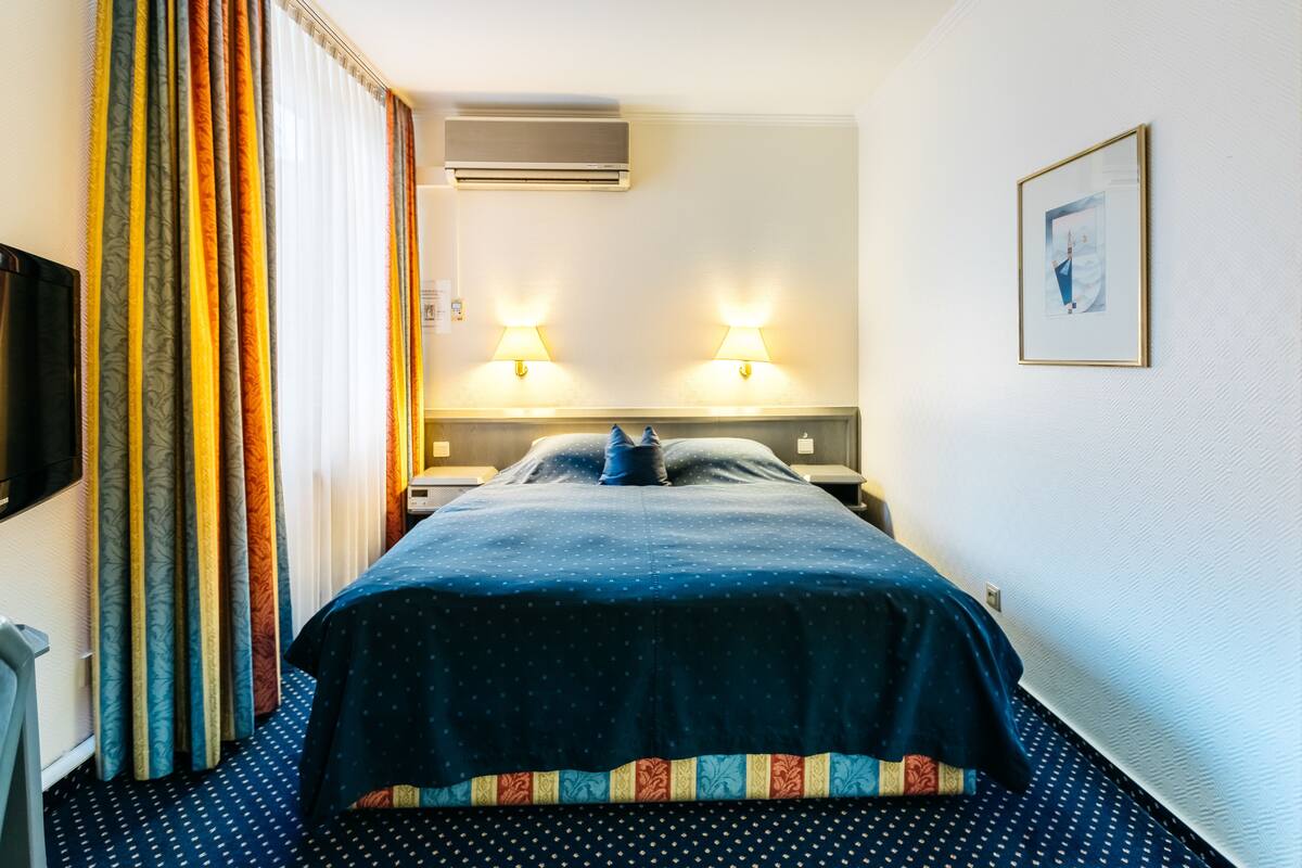 Ein Hotelzimmer mit einem Bett, zwei Nachttischlampen, einer Klimaanlage und einem gerahmten Bild an der Wand.