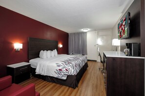 A hotel room with a bed, a desk, a chair, a TV, and a painting on the wall. - Red Roof Inn Gadsden (Gadsden)