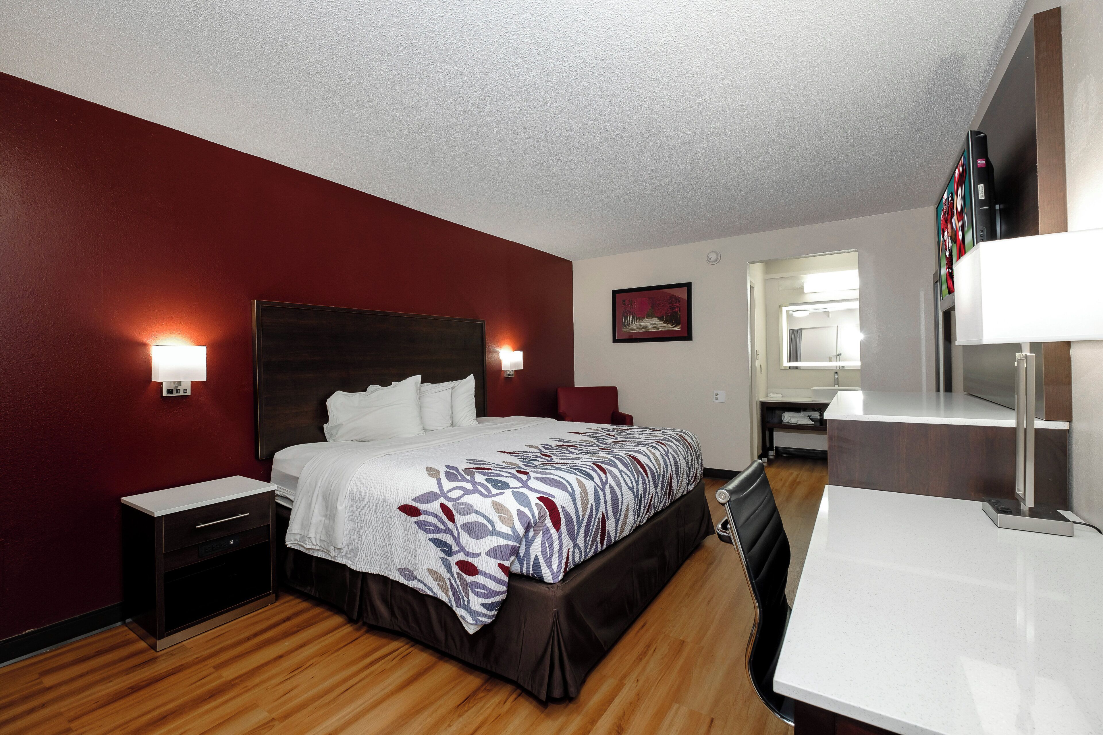 Una habitación de hotel con una cama grande, mesitas de noche, un escritorio y un espejo.
