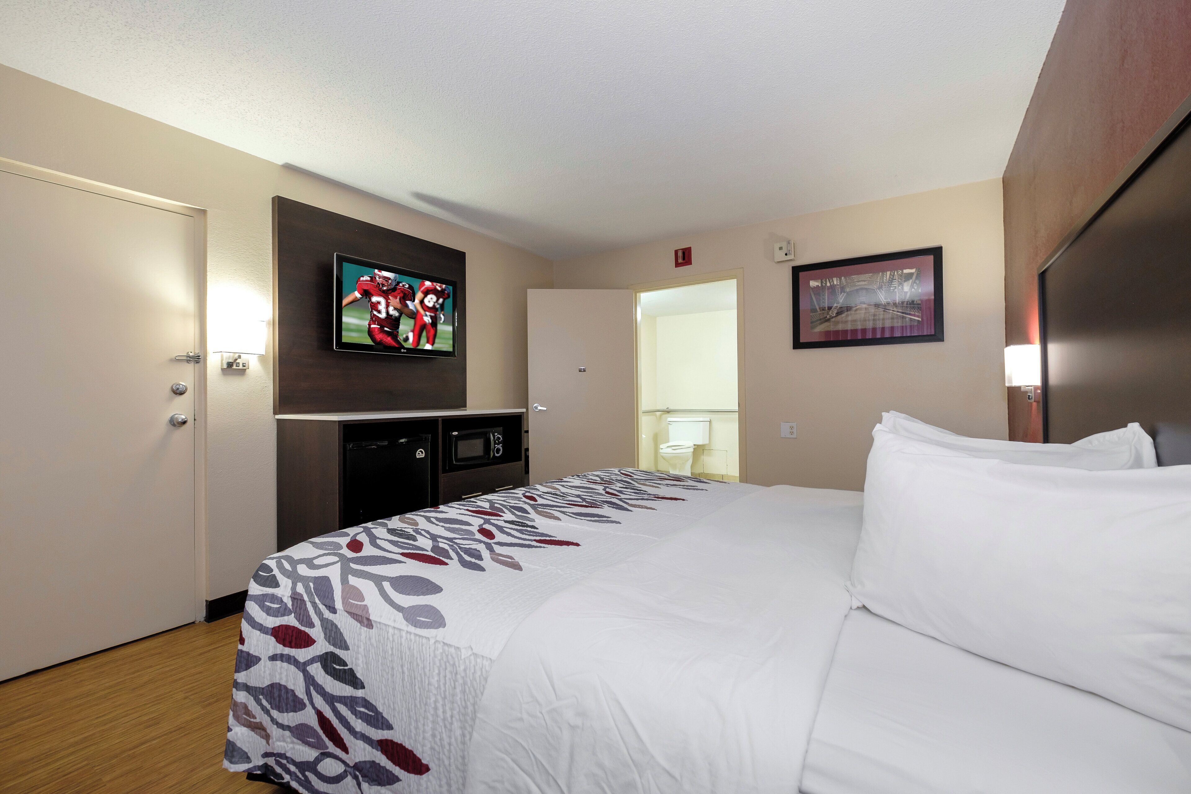 A hotel room with a bed, a television mounted on the wall, a microwave, and a small cabinet.