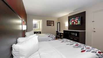 A hotel room with two beds, a desk, a television, and a door.