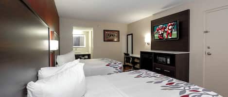 Quarto de hotel com duas camas, uma escrivaninha, televisão e uma porta.