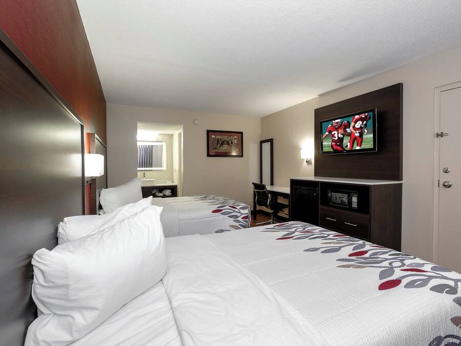 A hotel room with two beds, a desk, a television, and a door.