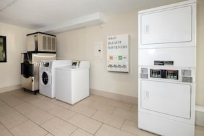 A laundry room with a front-loading washer, a top-loading dryer, and a wall-mounted air conditioning unit. - Red Roof Inn Gadsden (Gadsden)