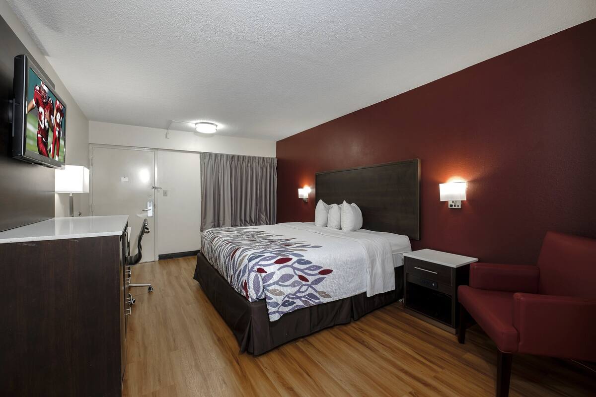 Una habitación de hotel con una cama, mesita de noche, lámpara y una silla roja.