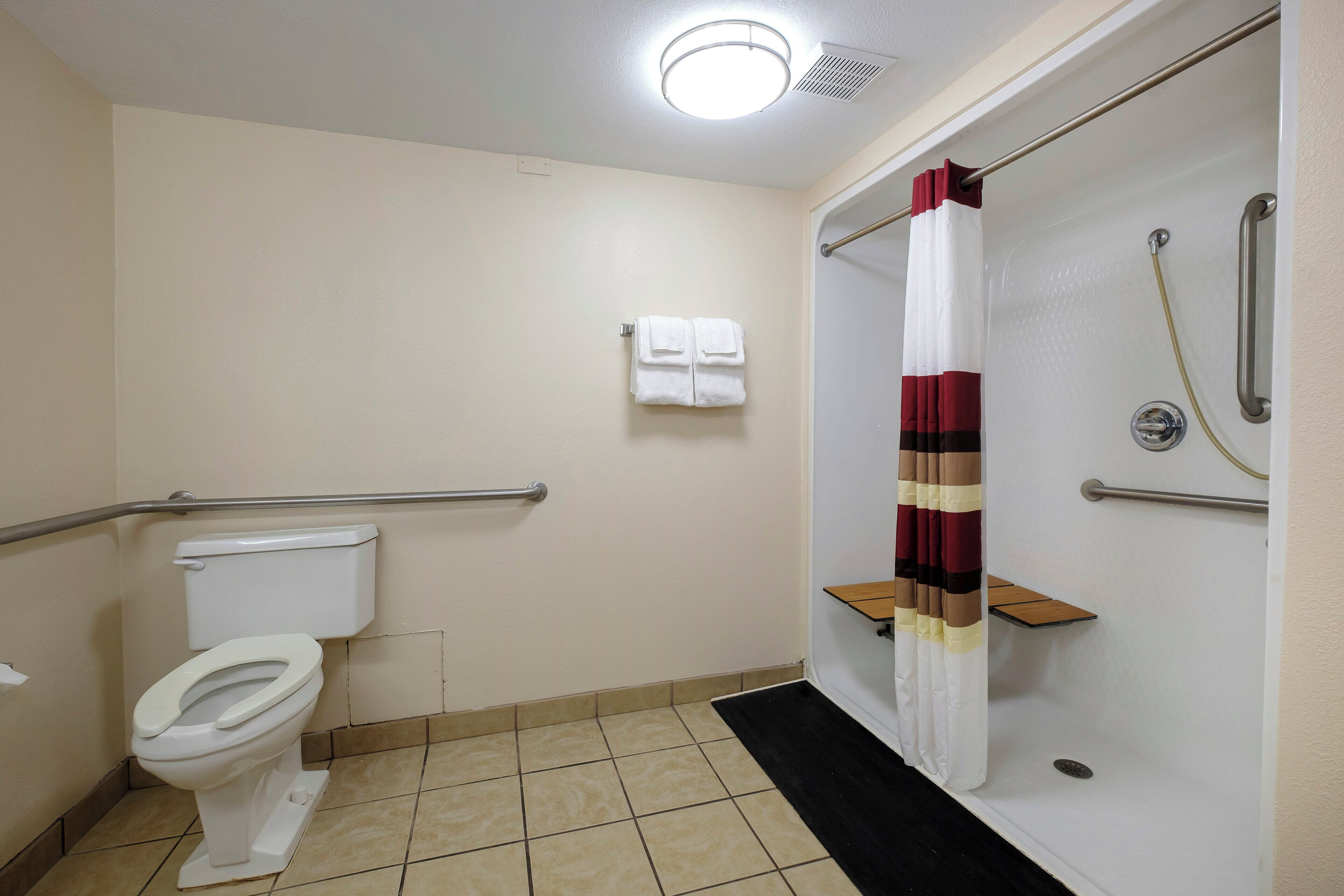 A bathroom with a toilet, a shower with a safety grab bar, and a towel rack.