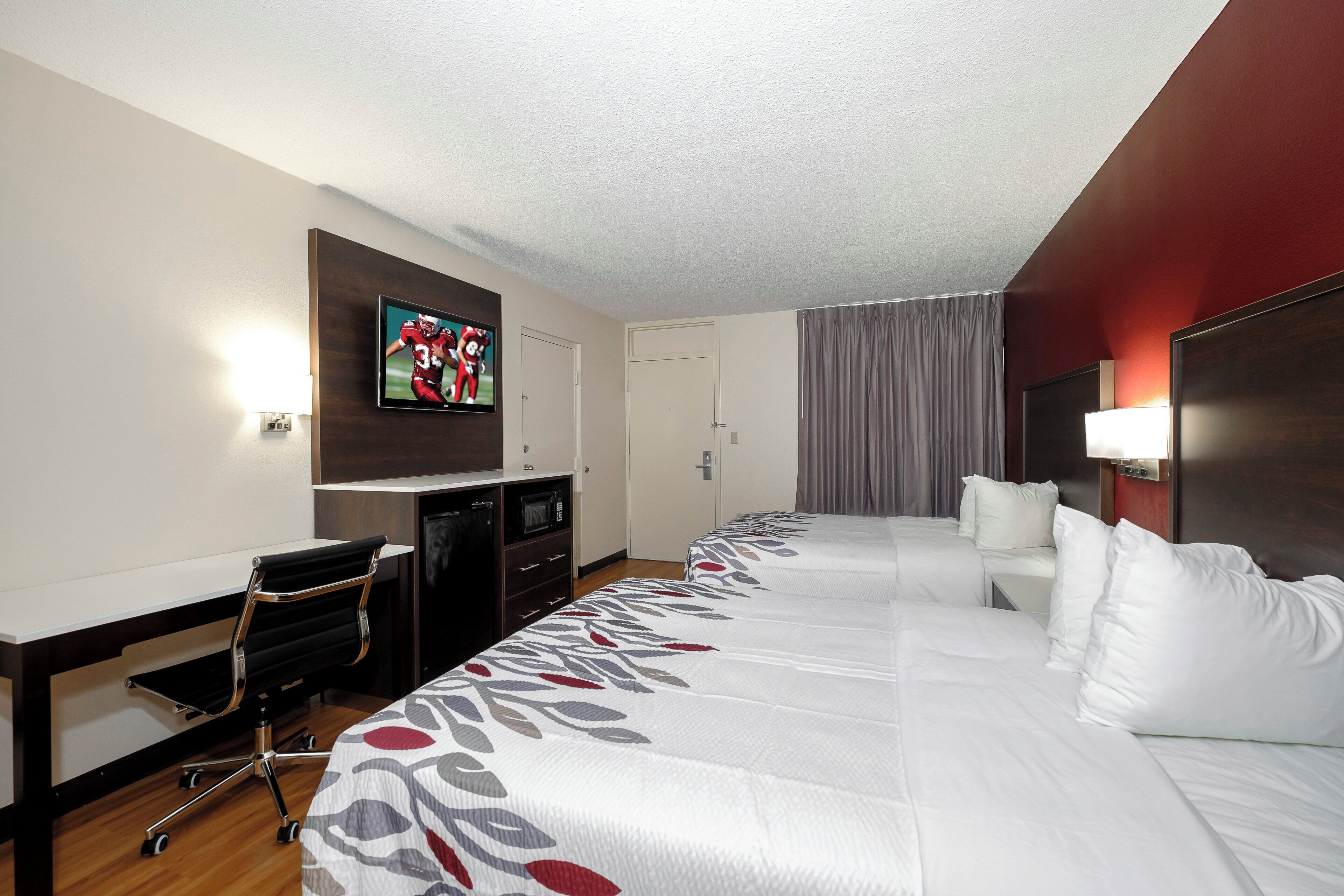 A hotel room with a large bed, a television, a desk with a chair, and a microwave.