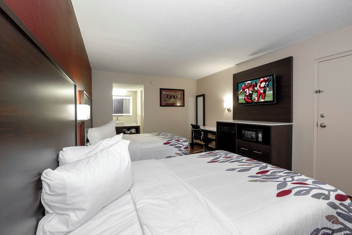 Ein Hotelzimmer mit zwei Betten, einem Fernseher, einem Schreibtisch und einer Mikrowelle.