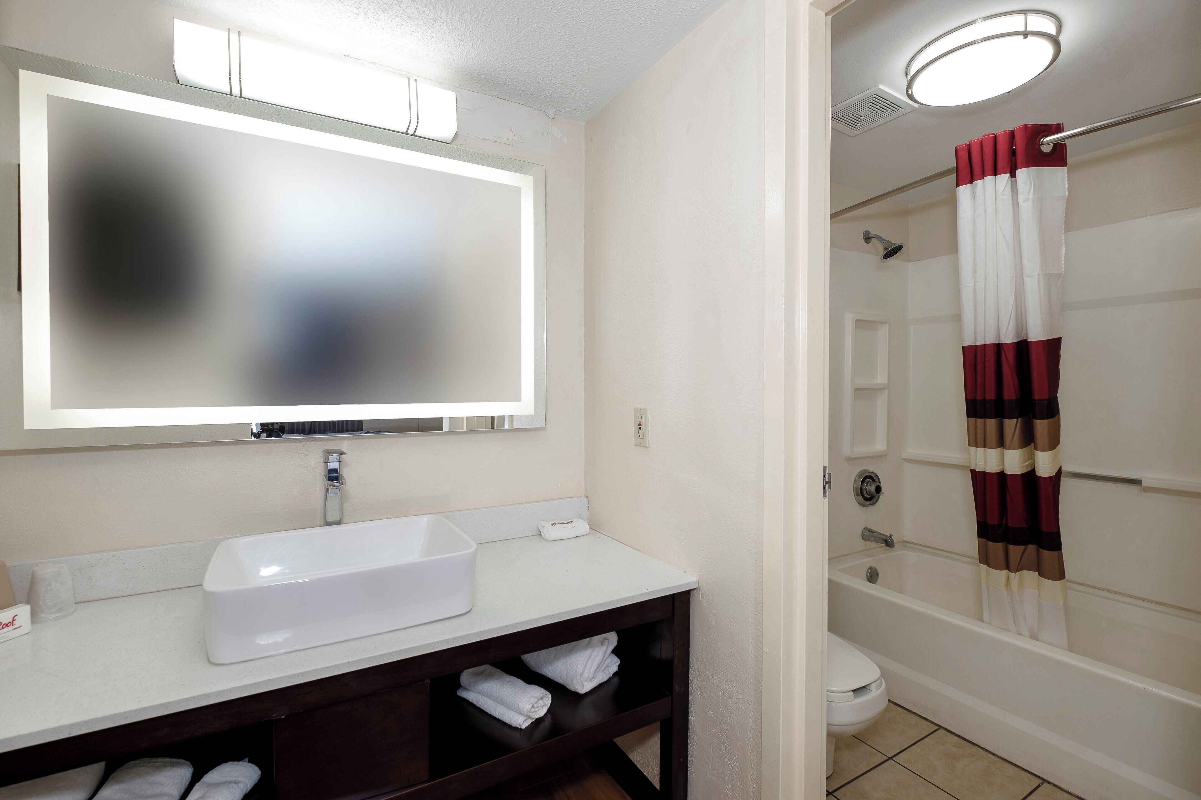 A bathroom with a white sink, a mirror, a shower with a striped curtain, and a toilet.