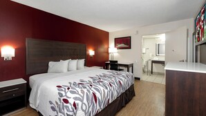 A hotel room with a large bed, bedside tables, a desk, and a bathroom visible through an open door. - Red Roof Inn Gadsden (Gadsden)