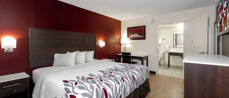 A hotel room with a large bed, bedside tables, a desk, and a bathroom visible through an open door.