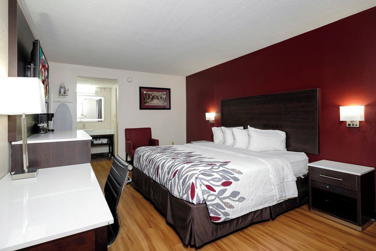 Ein Hotelzimmer mit Bett, Nachttischen, Schreibtisch, Stuhl, Spiegel und Wandfernseher.