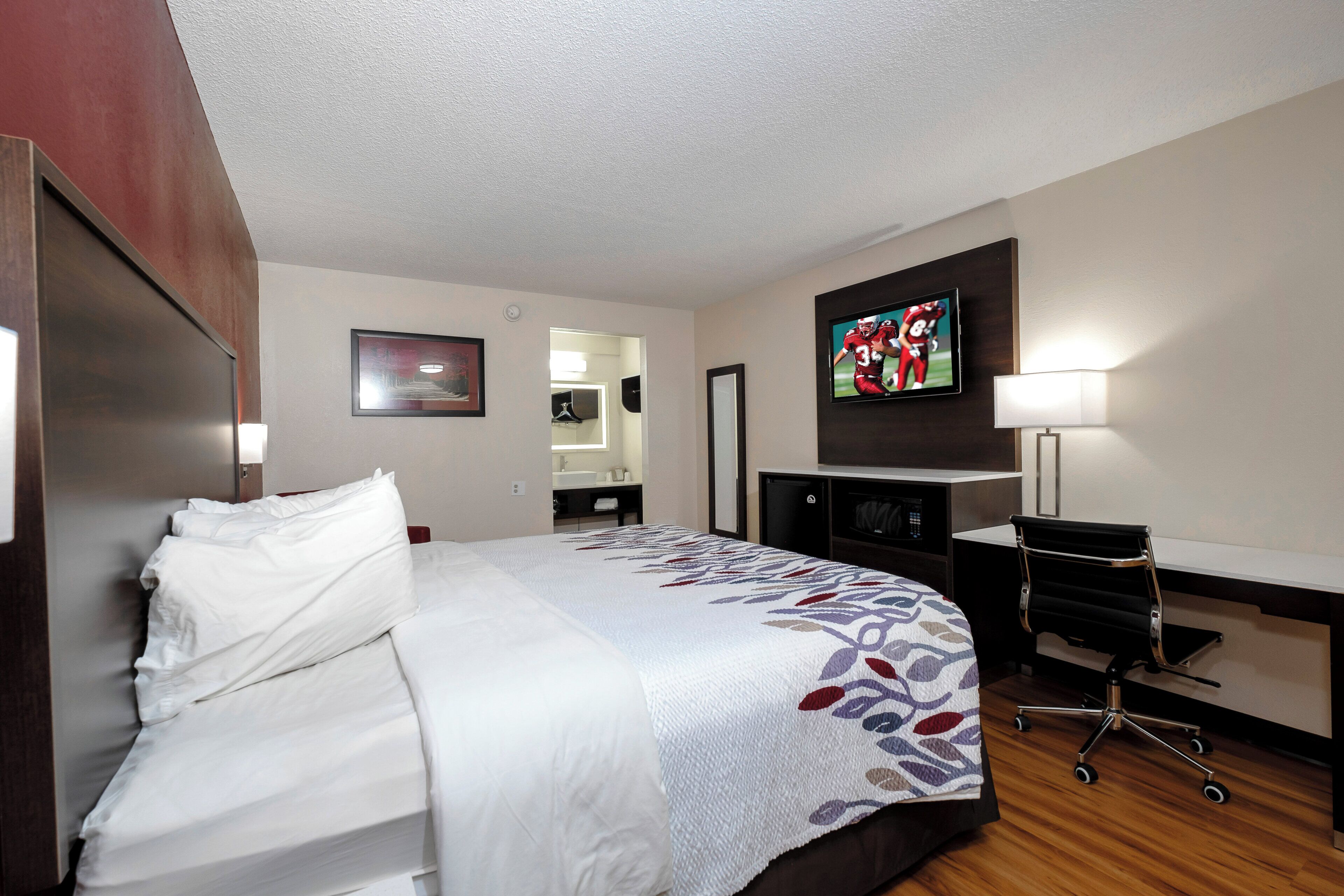 A hotel room with a bed, a desk, a television, and a chair.