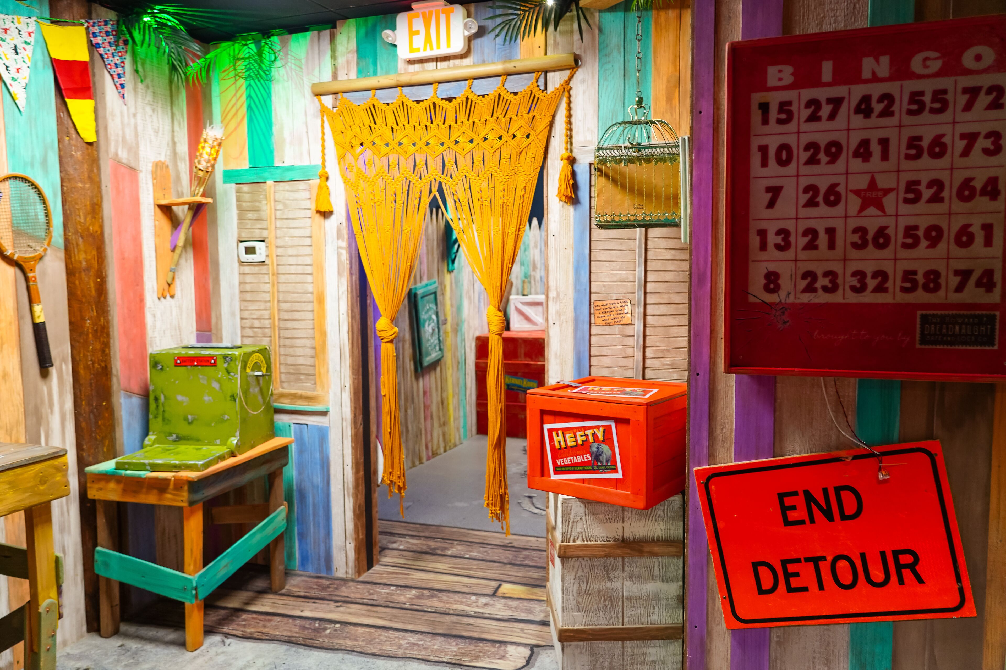 A colorful room with a wooden door, a green machine, a red box labeled 'Hefty Vegetables', and a 'Bingo' game board.