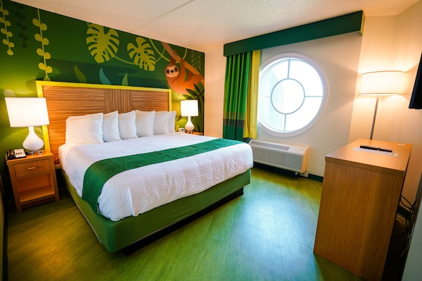 A hotel room with a large bed, two bedside tables with lamps, a round window, and a green-themed wall mural.