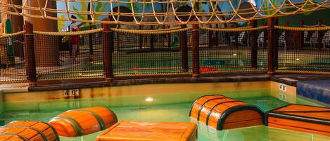 An indoor water play area with a rope bridge, wooden barrels, and a netted enclosure.