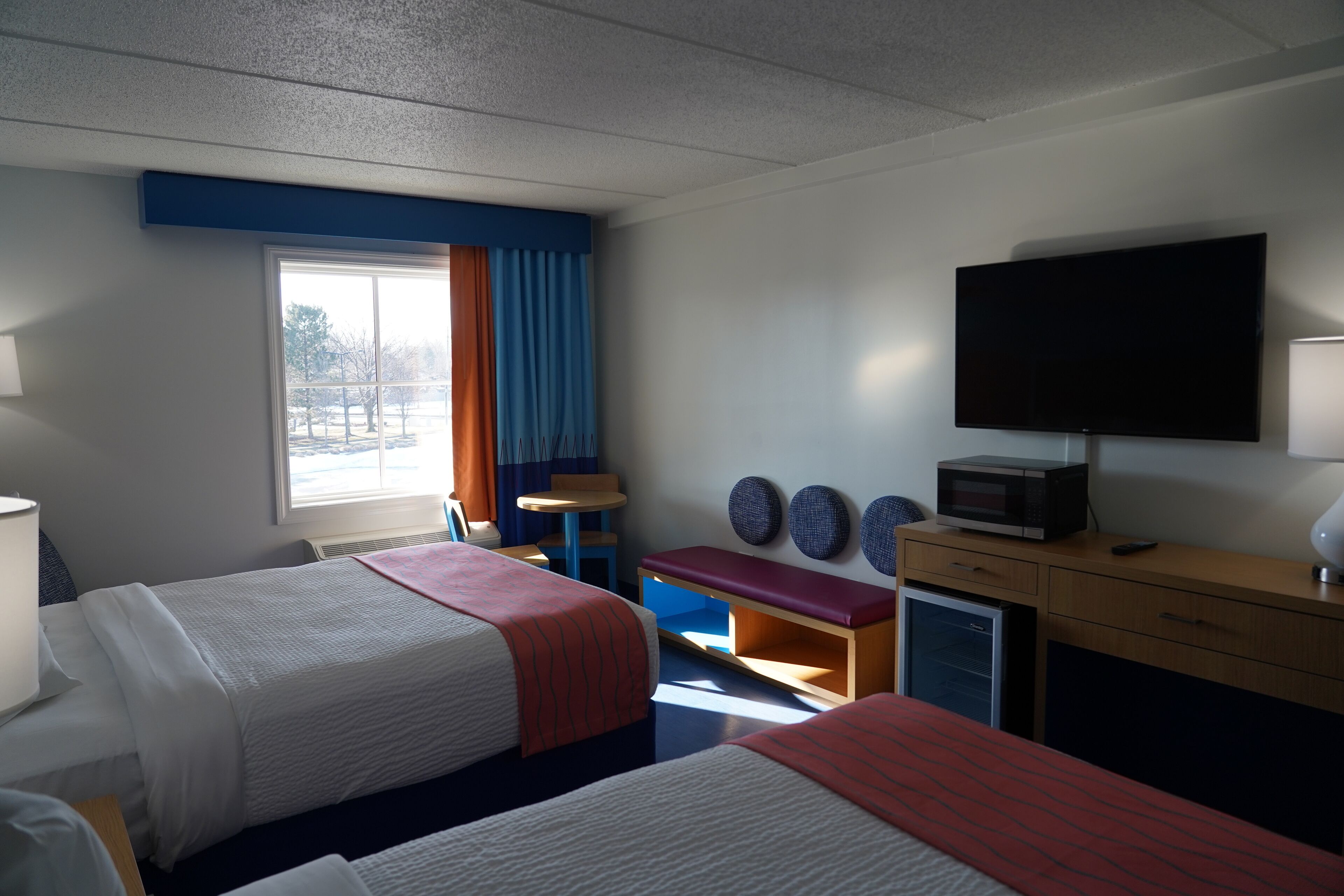 A hotel room with two beds, a TV, a microwave, a desk, and a window with curtains.
