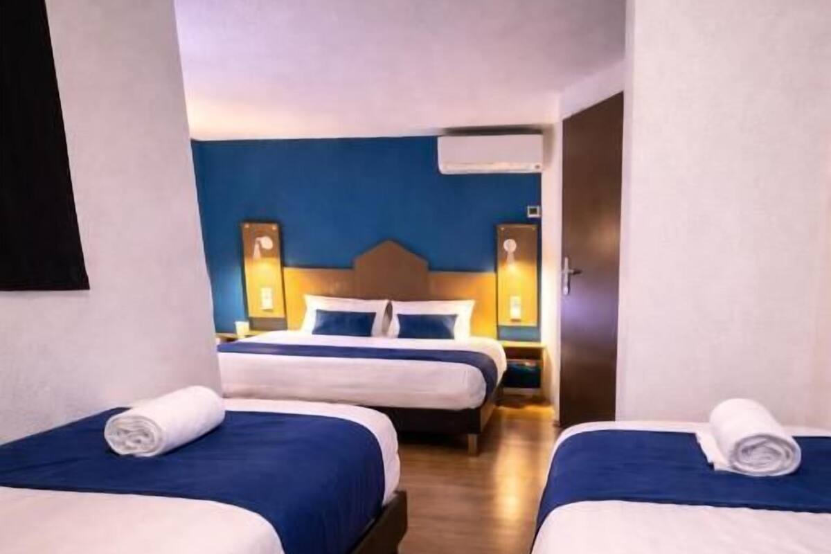 A hotel room with three single beds, wooden flooring, and a blue accent wall.