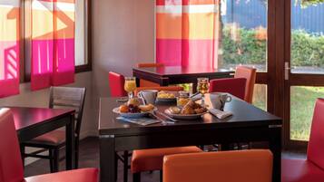 A dining area with a table set for breakfast, including plates of fruit, pastries, and a cup of coffee.