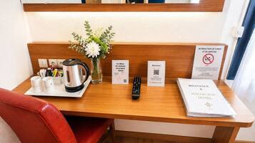 A hotel desk with a coffee maker, mug, remote control, and welcome sign.
