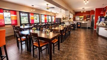 Een restaurant met meerdere eettafels en stoelen, een keuken en grote ramen met rode gordijnen.