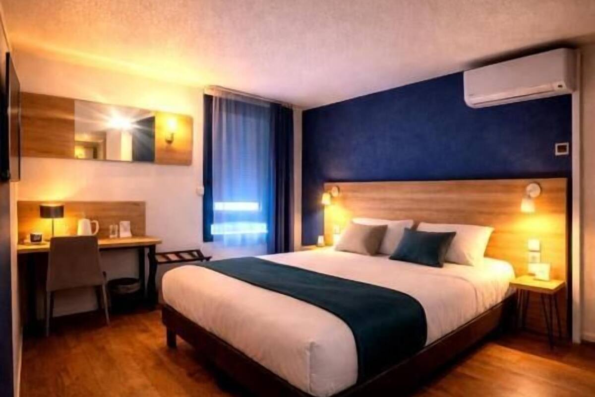 A hotel room with a bed, desk, chair, and a small table.