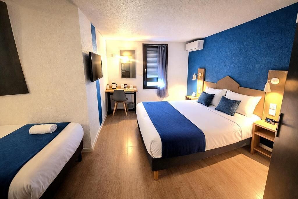 Habitación de hotel con dos camas, un escritorio, una silla, un televisor y una ventana con cortinas.