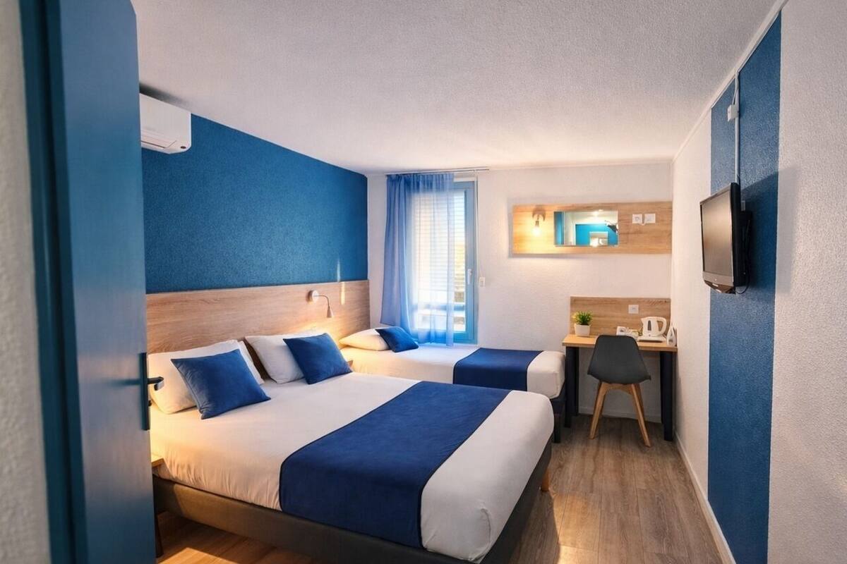 A hotel room with two beds, a desk, a chair, a TV, and a window with curtains.