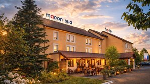 Un hôtel avec une enseigne indiquant « Macon Sud Hotel » et des tables à l’extérieur.