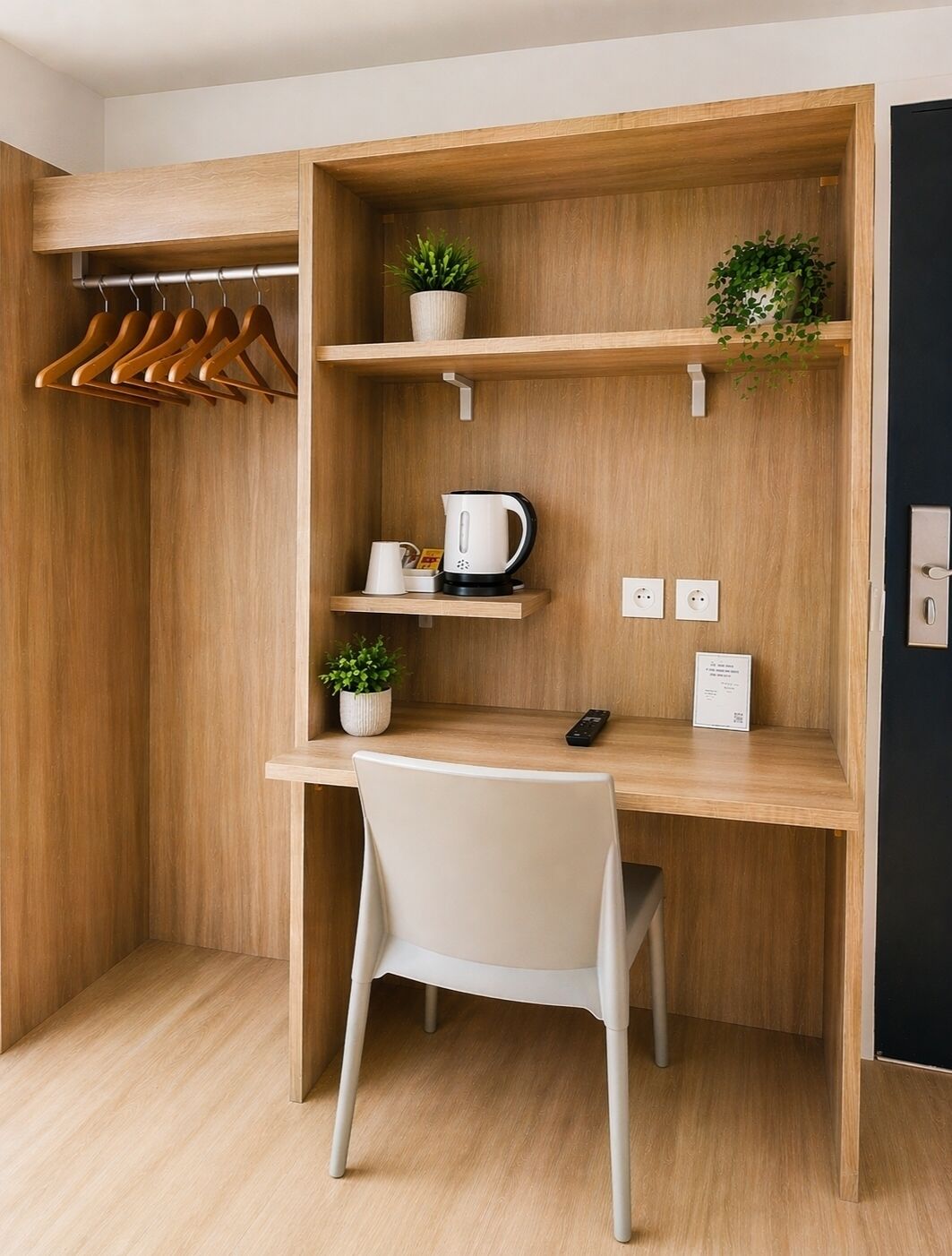 Ein kleines Zimmer mit einem Holztisch, einem Stuhl, einem Wasserkocher, einer Fernbedienung und einem Blumentopf.