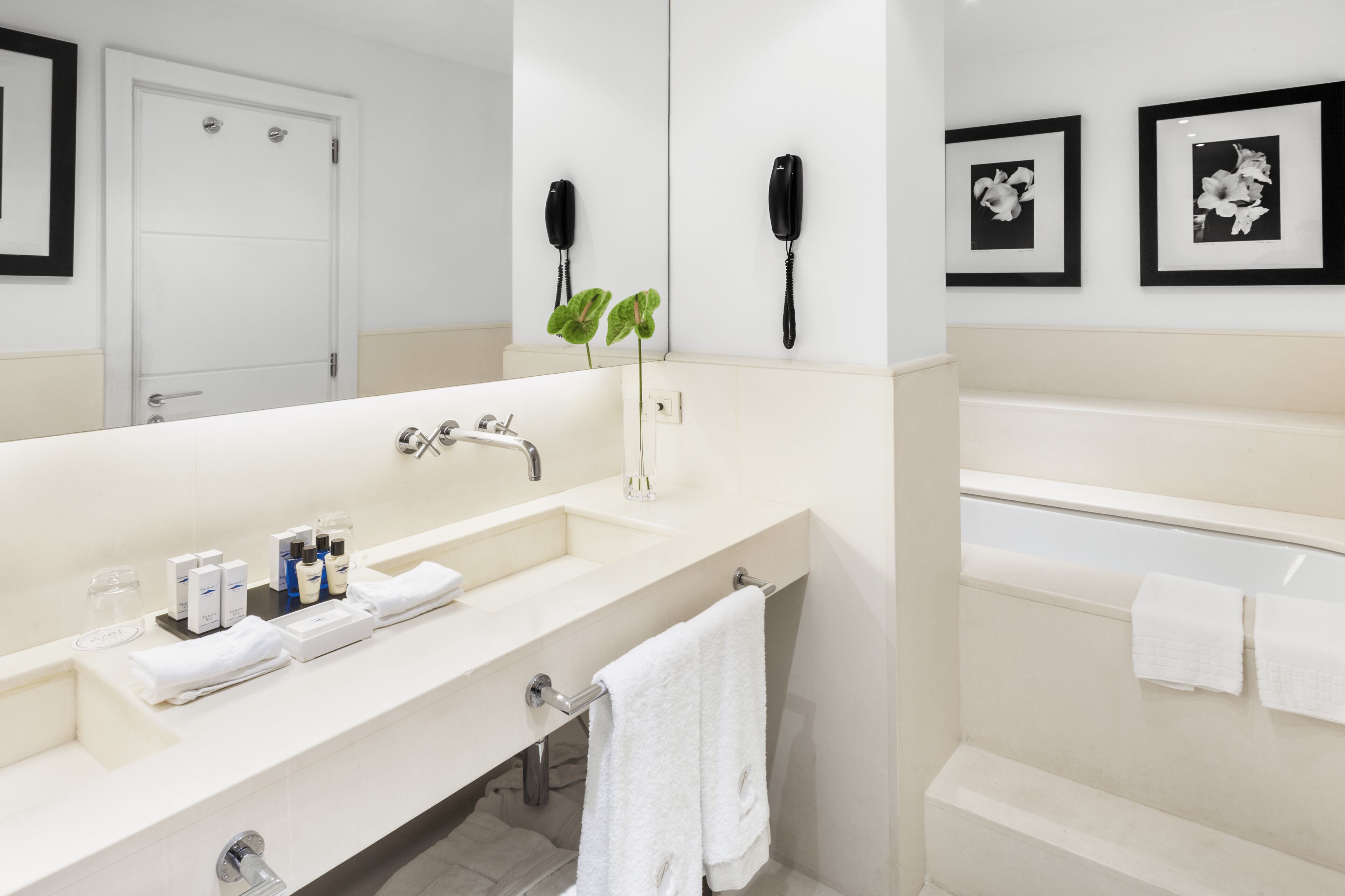Een moderne badkamer met een grote wastafel, een spiegel, een telefoon en bloemkunst in een lijst aan de muur.