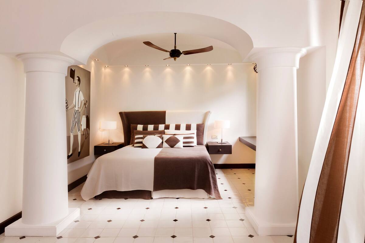 A bedroom with a bed, nightstands, a ceiling fan, and a wall-mounted artwork.