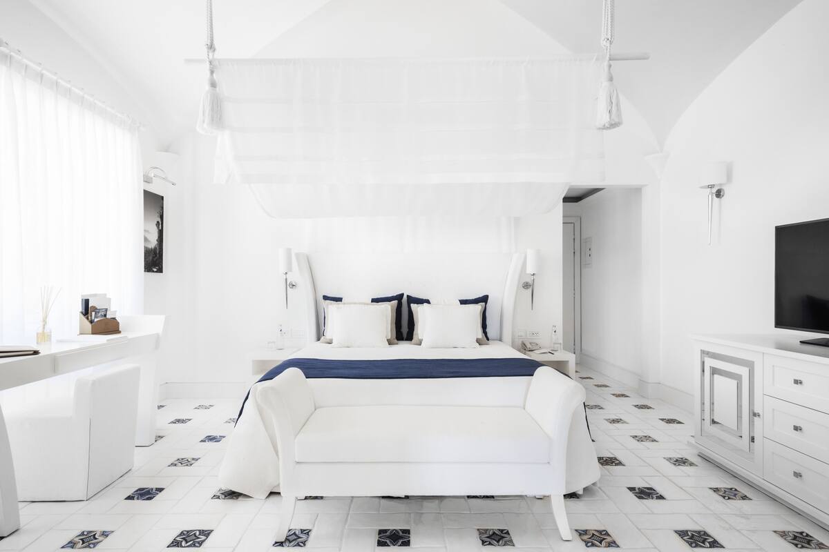 A modern bedroom with a bed, white furniture, and patterned floor tiles.
