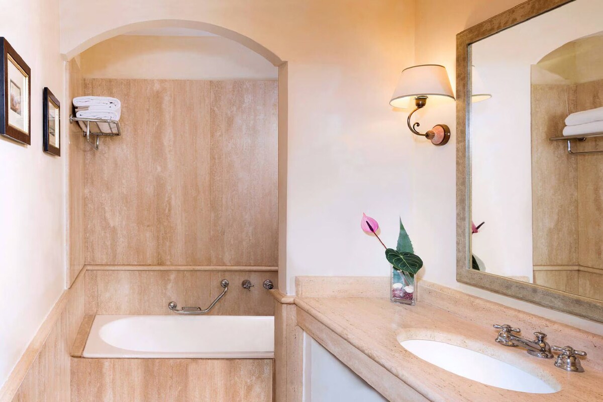 A bathroom with a bathtub, a sink, a mirror, a towel rack, and a small plant.