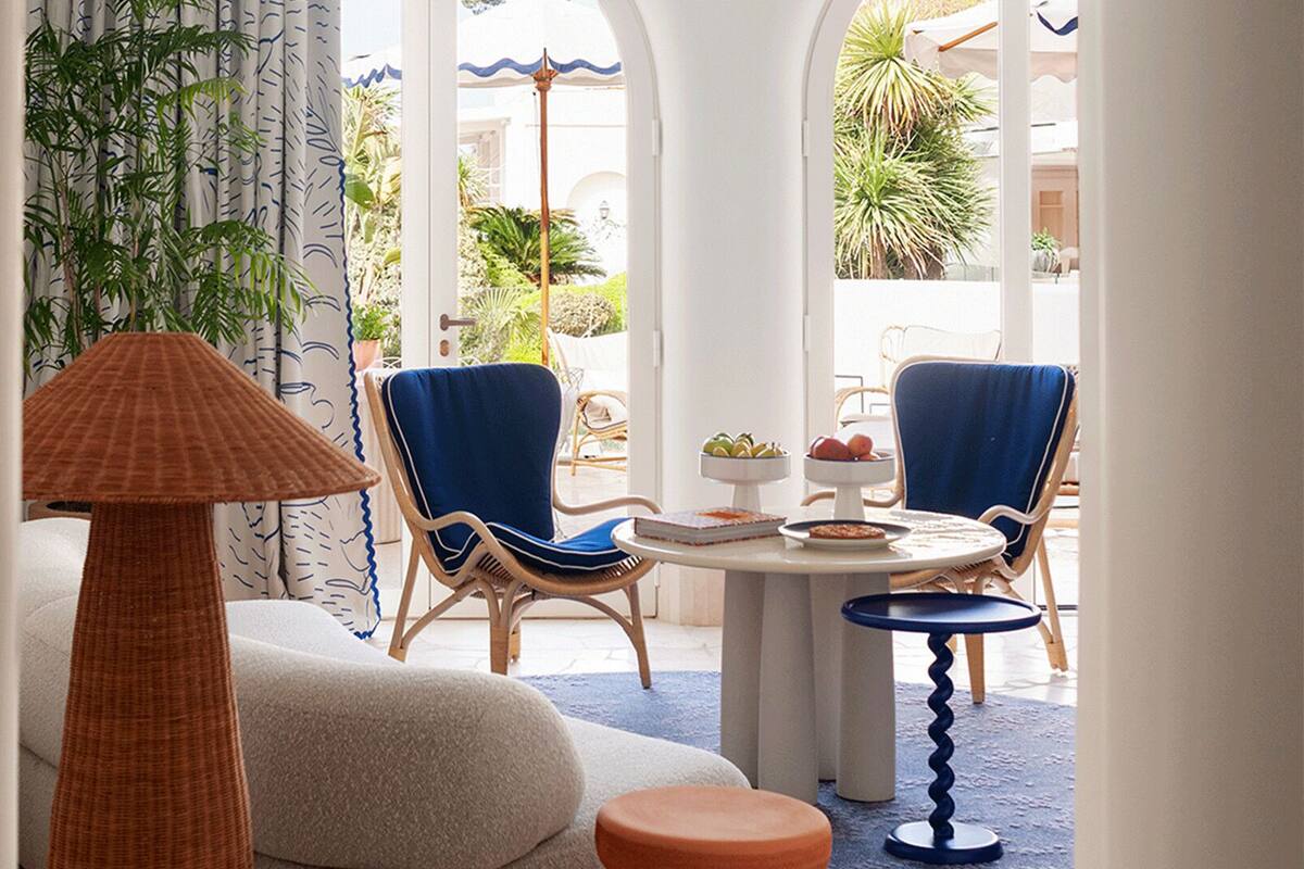 A room with a round table, two chairs, a lamp, and a view of the outdoors.