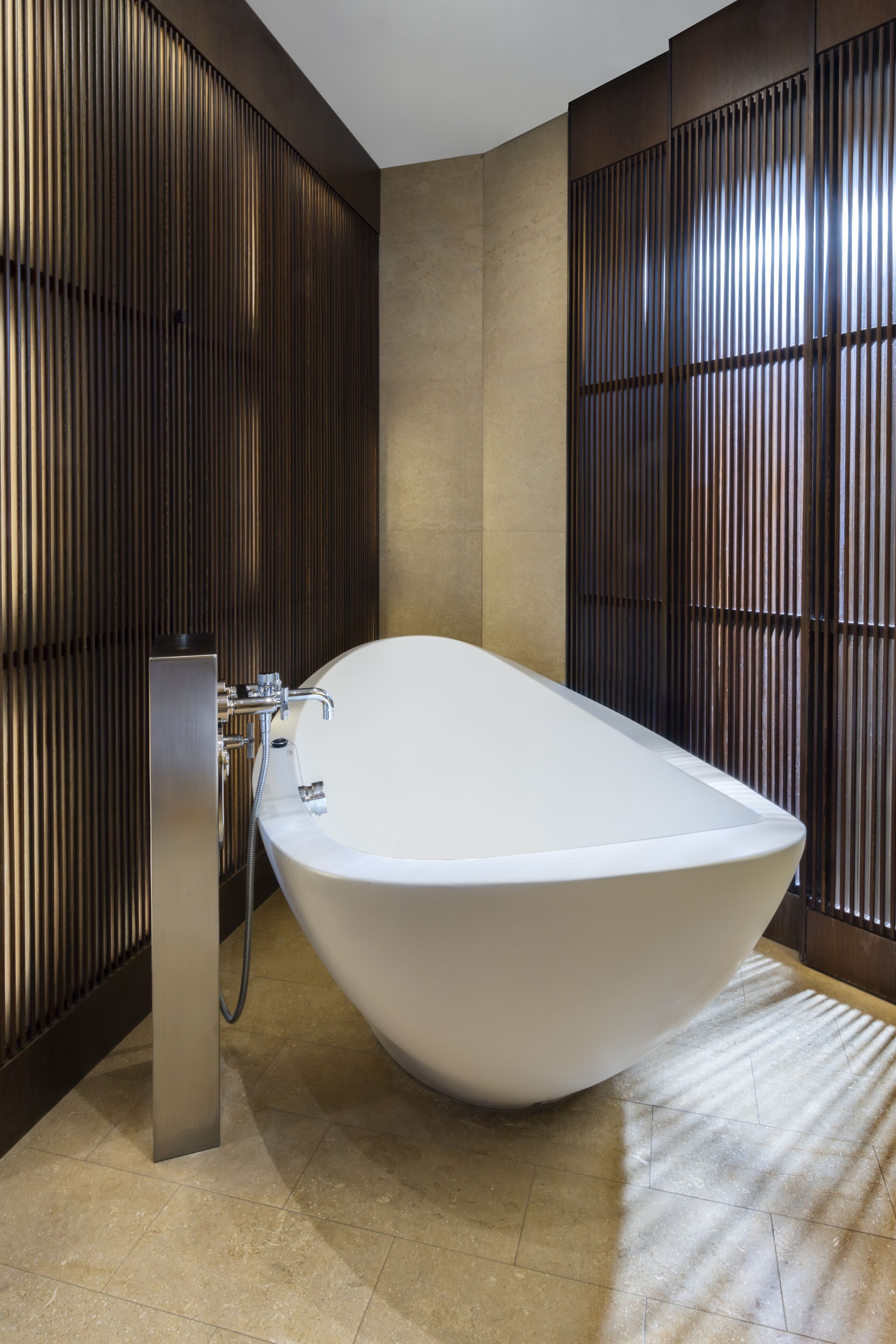 A modern bathroom with a freestanding bathtub, vertical wooden paneling, and a tiled floor.