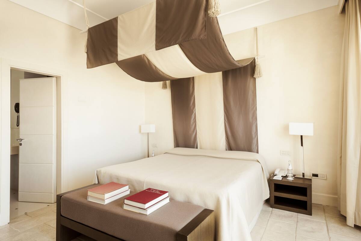 A hotel room with a large bed, bedside tables, and a small bedside table with a lamp.