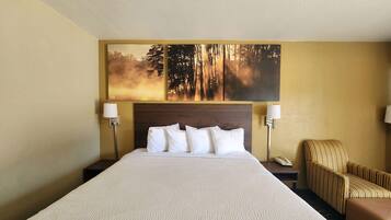 A hotel room with a large bed, two bedside tables, a chair, and a wall-mounted painting of a forest scene.