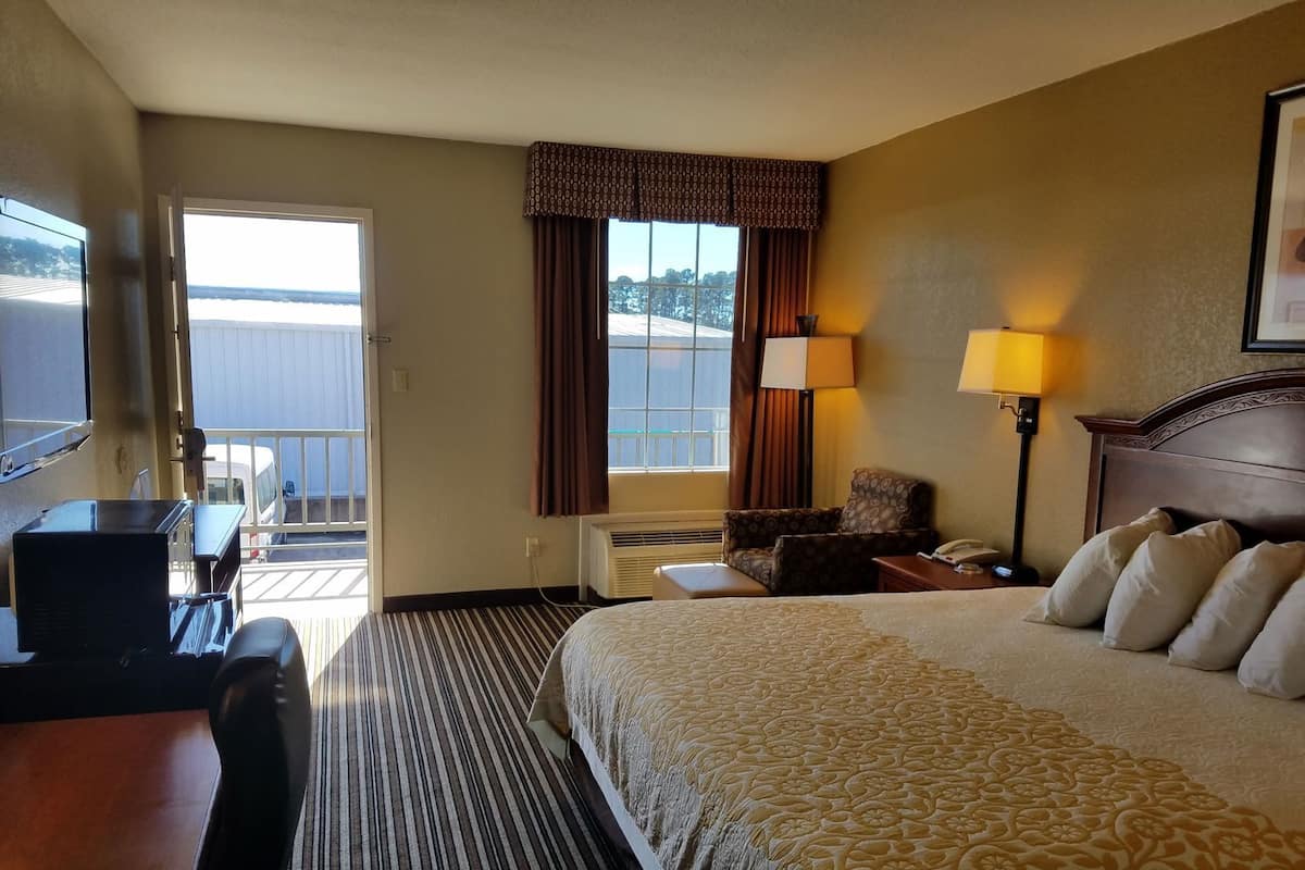 Habitación de hotel con cama, escritorio, silla, lámpara y vistas al exterior.