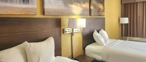A hotel room with two beds, a nightstand, a lamp, and a painting of a waterfall.